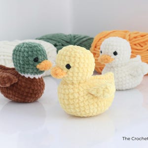 May include: Three crocheted ducklings in brown, yellow, and white, each with an orange beak and black eyes. The ducks are in front of balls of yarn in white, green, and orange. The Crochet Code is written in the bottom right corner.