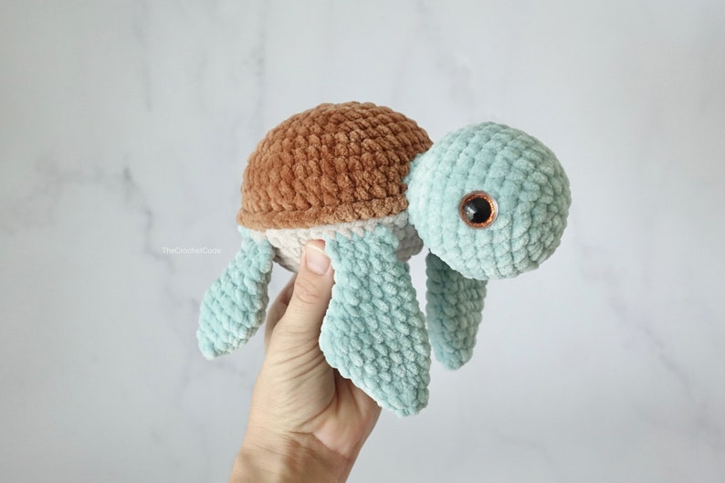 K&ouml;nnte beinhalten: Ein geh&auml;keltes Schildkr&ouml;tenspielzeug mit einer braunen und beigefarbenen Schale und einem hellblauen K&ouml;rper. Die Schildkr&ouml;te hat gro&szlig;e braune Augen.