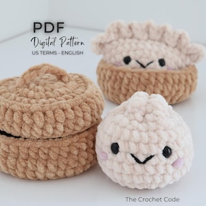 May include: A crochet pattern PDF titled PDF Digital Pattern US TERMS - ENGLISH and The Crochet Code. The image features a tan crocheted lidded container, a tan crocheted dumpling in a basket, and a white crocheted dumpling with a smiling face.