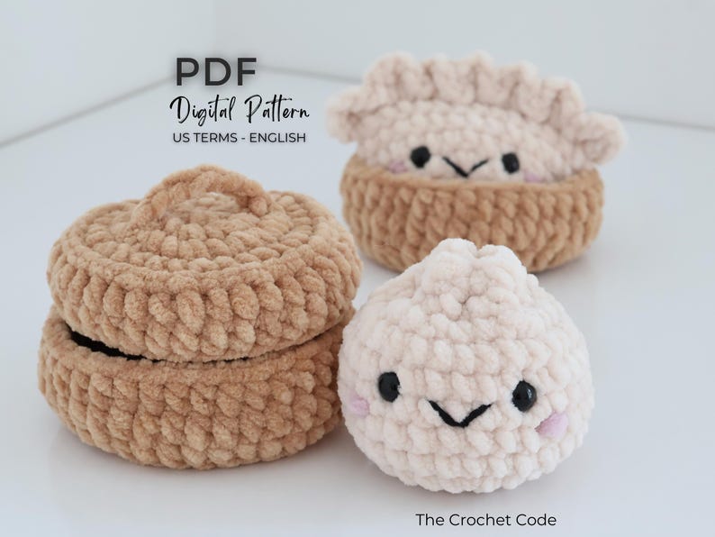 May include: A crochet pattern PDF titled PDF Digital Pattern US TERMS - ENGLISH and The Crochet Code. The image features a tan crocheted lidded container, a tan crocheted dumpling in a basket, and a white crocheted dumpling with a smiling face.