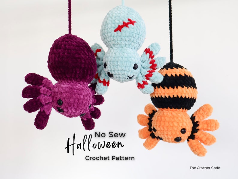 Hung upside down from a height this image displays 3 spiders purple, green and orange with their crocheted legs spread out touching each other.