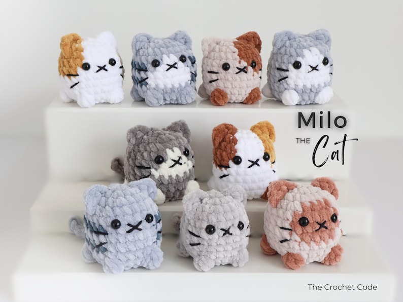 May include: A collection of handmade crochet cat figurines in various colors, including white, gray, and brown. Each cat has black eyes and whiskers. The text "Milo the Cat" and "The Crochet Code" are also visible.