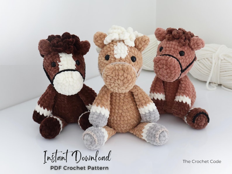 Three plush crochet horse toys in shades of brown, tan, and white sit side-by-side. Each horse has a unique color pattern and black eyes. The text "Instant Download PDF Crochet Pattern" is visible at the bottom. The Crochet Code is also visible.