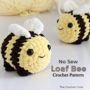 Può includere: Due piccole api rotonde realizzate all'uncinetto con filato giallo morbido e marrone scuro, con ali bianche e occhi in plastica nera. Il testo "No Sew Loaf Bee Crochet Pattern" e "The Crochet Code" è stampato nell'angolo in basso a destra.