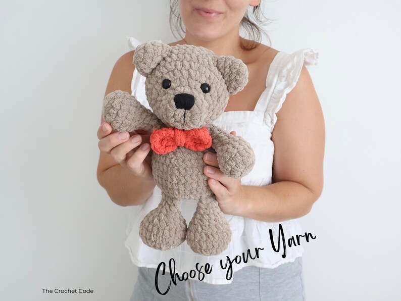 May include: A crocheted teddy bear with a brown body and a red bow tie. The bear is being held by a person. The text "Choose your yarn" is written in black cursive on the bottom of the image.