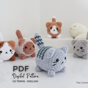 May include: A collection of handmade crochet cat figurines in various colors, including brown, white, and gray. Each cat has a unique design, with black whiskers and facial details. The image also includes yarn and text that says "PDF Digital Pattern".