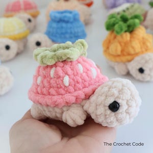May include: A collection of handmade crochet turtles, each with a unique fruit-themed shell. The featured turtle has a pink strawberry shell with white accents and a green leafy top. Other turtles have shells resembling a pineapple, lemon, and watermelon.