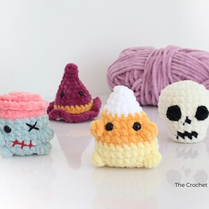 May include: A selection of handmade crochet Halloween figures. Includes a blue and pink monster, a purple witch hat, a candy corn, and a white skull. A ball of lavender yarn is in the background. The Crochet Code is written on the bottom right.
