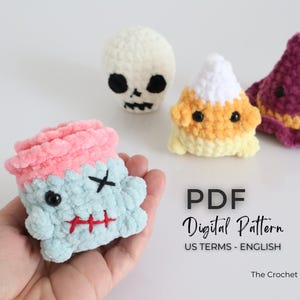 May include: A selection of handmade crochet Halloween plush toys. The toys include a zombie, a skull, a candy corn, and a witch's hat. The zombie is light blue with a pink top, black cross-eyes, and a red stitched mouth. The candy corn is yellow, orange, and white.