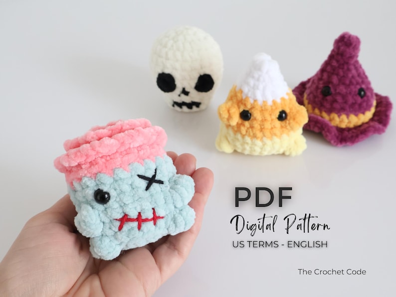 May include: A selection of handmade crochet Halloween plush toys. The toys include a zombie, a skull, a candy corn, and a witch's hat. The zombie is light blue with a pink top, black cross-eyes, and a red stitched mouth. The candy corn is yellow, orange, and white.