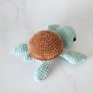 K&ouml;nnte beinhalten: Ein geh&auml;keltes Schildkr&ouml;tenspielzeug mit einer braunen Schale und einem hellblauen K&ouml;rper. Die Schildkr&ouml;te hat schwarze Augen und liegt auf einer wei&szlig;en Oberfl&auml;che.