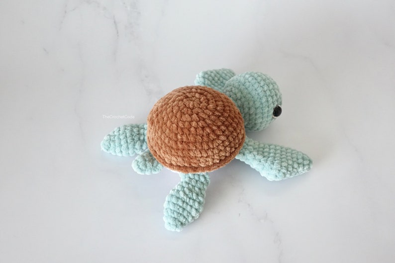 K&ouml;nnte beinhalten: Ein geh&auml;keltes Schildkr&ouml;tenspielzeug mit einer braunen Schale und einem hellblauen K&ouml;rper. Die Schildkr&ouml;te hat schwarze Augen und liegt auf einer wei&szlig;en Oberfl&auml;che.
