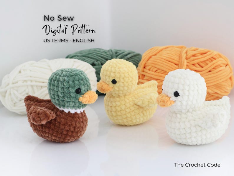 May include: Three crocheted ducklings in yellow, white, and brown with orange beaks and black eyes. The ducks are in front of balls of yarn in white, green, and orange. The text "No Sew Digital Pattern" is at the top.