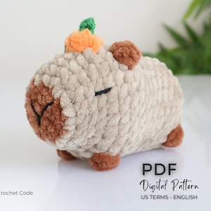 K&ouml;nnte beinhalten: Ein geh&auml;keltes Amigurumi-Spielzeug in Form eines Schweins mit einem kleinen orangefarbenen K&uuml;rbis auf dem Kopf. Das Schwein ist beige mit braunen Akzenten um die Augen und die Nase. Das Spielzeug ist aus weichem, flauschigem Garn gefertigt. Der Text "PDF Digital Pattern US TERMS - ENGLISH" ist am unteren Rand des Bildes sichtbar.