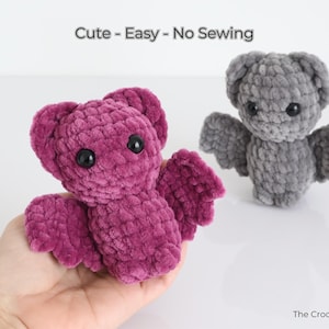 K&ouml;nnte beinhalten: Zwei geh&auml;kelte Fledermaus-Pl&uuml;schtiere. Eines wird in einer Hand gehalten und hat eine tiefmagentafarbene Farbe. Das andere ist grau. Beide haben schwarze Augen und Fl&uuml;gel. Der Text "Cute - Easy - No Sewing" steht oben.