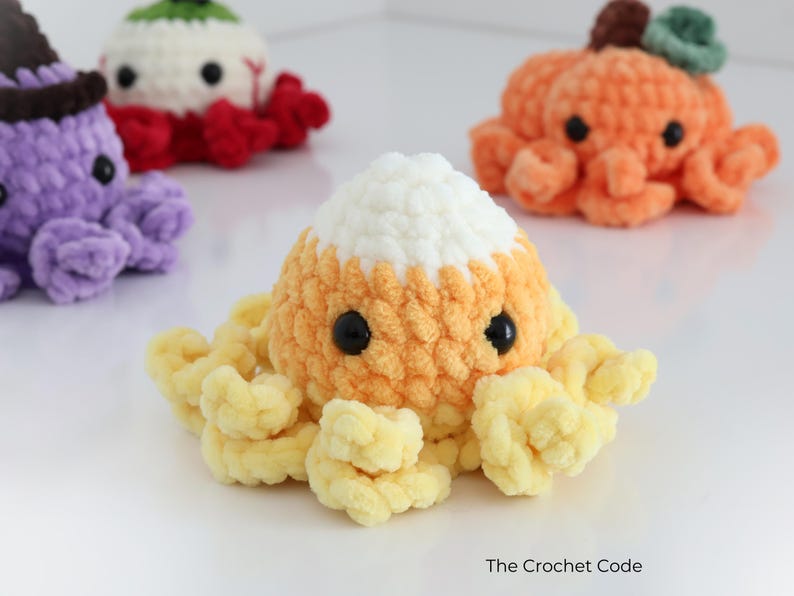 Puede incluir: Tres juguetes de pulpo de peluche tejidos a ganchillo con ojos de seguridad negros. Uno es naranja y amarillo como un caramelo de ma&iacute;z, uno es morado con un sombrero marr&oacute;n oscuro y uno es naranja con un tallo verde. El texto The Crochet Code aparece.
