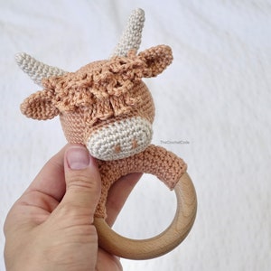 May include: A crocheted cow rattle with a wooden ring. The cow is brown and white with a white face and brown spots. The rattle is ideal for a baby or toddler.