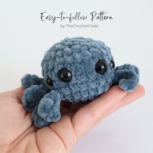 May include: A handmade, blue crocheted octopus with large black eyes and eight tentacles. The text "Easy-to-follow Pattern" and "by TheCrochetCode" are visible in the image. The octopus is held in a person's hand.