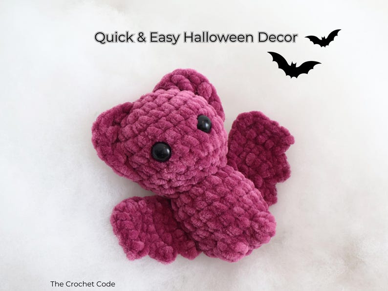 K&ouml;nnte beinhalten: Eine pl&uuml;schige, burgunderfarbene Fledermaus mit schwarzen Knopfaugen und Fl&uuml;geln. Der Text "Quick & Easy Halloween Decor" steht &uuml;ber der Fledermaus, mit zwei schwarzen Fledermaus-Silhouetten. The Crochet Code steht unten.