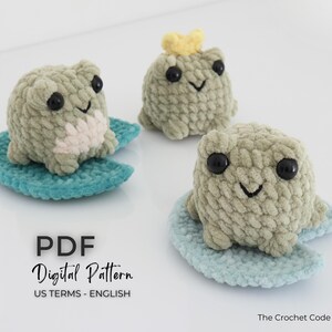 May include: Three handmade crochet frog toys in shades of green, each with black eyes and a smiling mouth. One frog wears a yellow crown. They sit on blue lily pads. The image includes the text "PDF Digital Pattern".