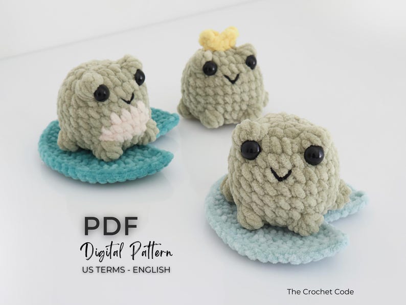 May include: Three handmade crochet frog toys in shades of green, each with black eyes and a smiling mouth. One frog wears a yellow crown. They sit on blue lily pads. The image includes the text "PDF Digital Pattern".