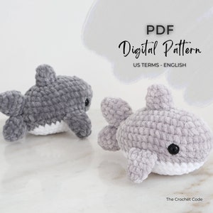 May include: Two plush, gray crocheted shark toys with white bellies and black eyes. The text "PDF Digital Pattern US TERMS - ENGLISH" is displayed above the sharks. The Crochet Code is written at the bottom.