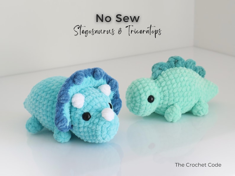 May include: Two crocheted dinosaur toys: a blue Triceratops with white horns and a teal Stegosaurus. The toys are handmade and have black safety eyes. The text "No Sew Stegosaurus & Triceratops" is at the top.