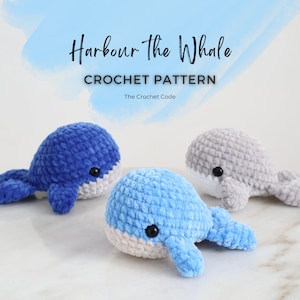 Op de afbeelding: Drie gehaakte walvisknuffels in tinten blauw en grijs, met witte buiken en zwarte ogen. De tekst "Harbour the Whale CROCHET PATTERN" staat boven de walvissen, met "The Crochet Code" eronder.
