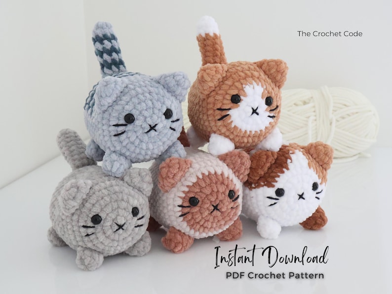 May include: A group of five crocheted cat toys in various colors, including gray, orange, and white. Each cat has black button eyes and embroidered details. The text "The Crochet Code" and "Instant Download PDF Crochet Pattern" are visible.