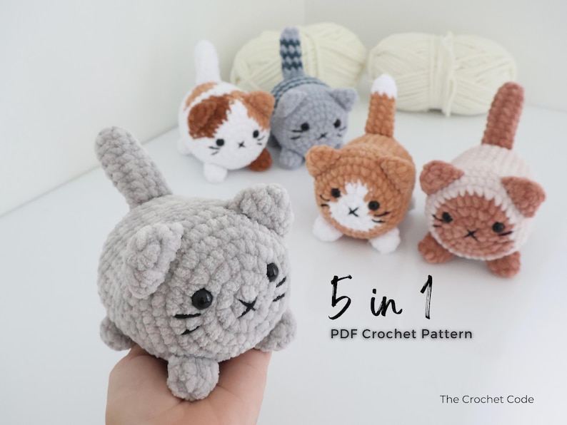 May include: A collection of five crocheted cat toys in various colors, including gray, brown, and orange, with white accents. Each cat has a unique pattern and facial expression. The image also includes the text "5 in 1 PDF Crochet Pattern".