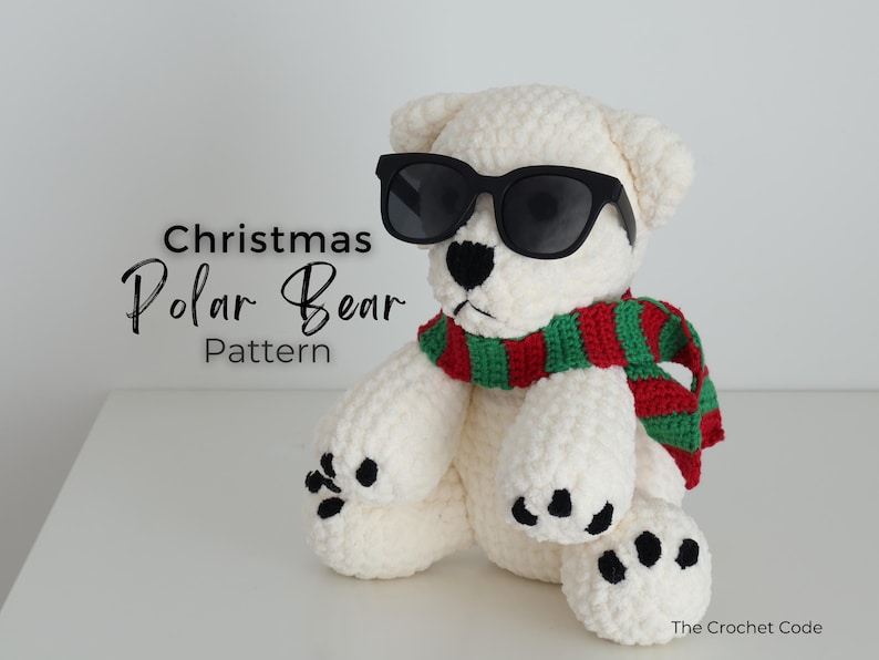 May include: A crocheted polar bear wearing black sunglasses and a red and green striped scarf. The bear has black paw pads and a black nose. Text on the image reads "Christmas Polar Bear Pattern".