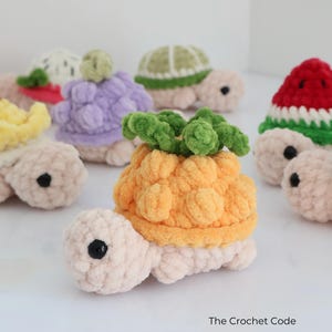 May include: A collection of handmade crochet turtles, each with a unique fruit-themed shell. The turtles feature a variety of colors, including yellow, purple, green, red, and blue. The turtles are made of soft, textured yarn and have black button eyes.