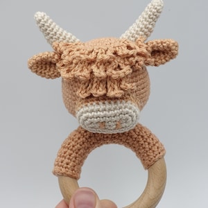 May include: A crocheted brown and white Highland cow rattle with a wooden ring.