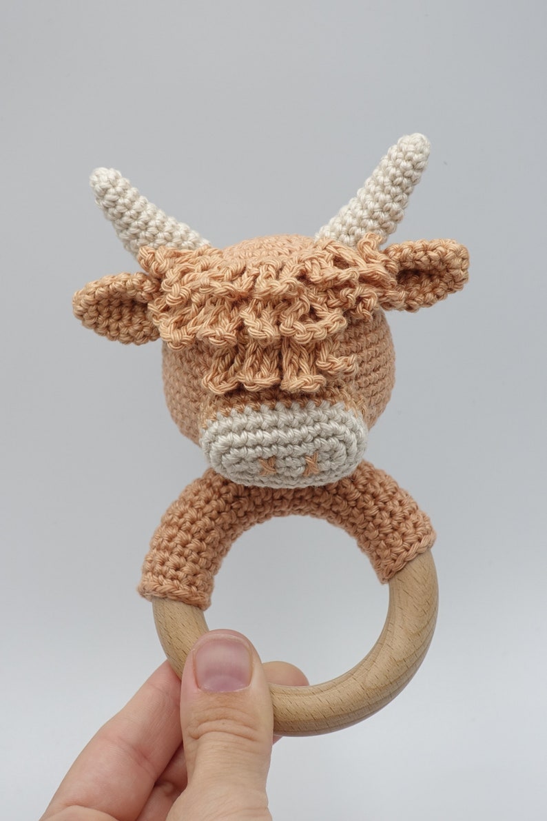May include: A crocheted brown and white Highland cow rattle with a wooden ring.