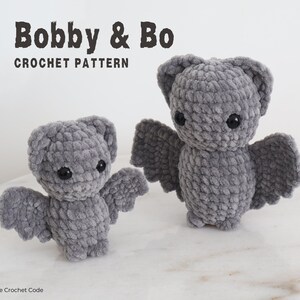 May include: Two gray crocheted bat plushies, one larger than the other, with black eyes. The smaller bat is on the left and the larger bat is on the right. The bats are on a gray surface. The text "Bobby & Bo CROCHET PATTERN" is at the top of the image.
