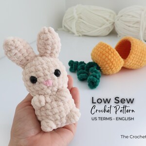 May include: A light beige crochet bunny with black eyes and a pink nose is held in a hand. Beside it are a crochet carrot and green carrot tops. The image also includes text that says "Low Sew Crochet Pattern".