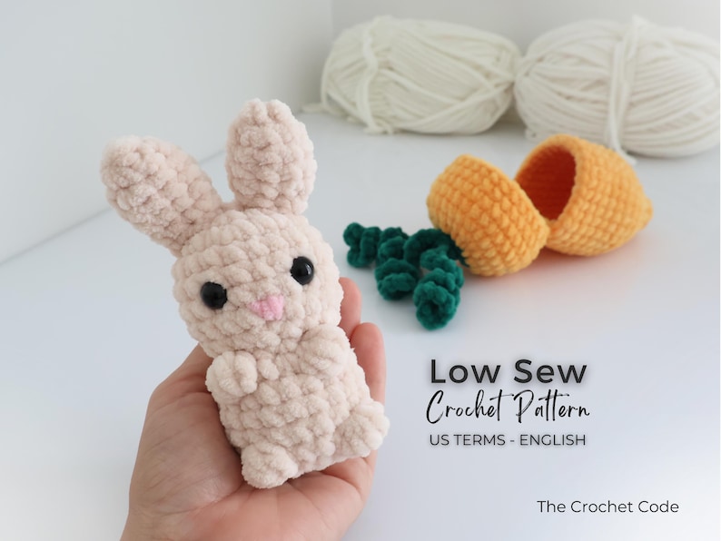 May include: A light beige crochet bunny with black eyes and a pink nose is held in a hand. Beside it are a crochet carrot and green carrot tops. The image also includes text that says "Low Sew Crochet Pattern".