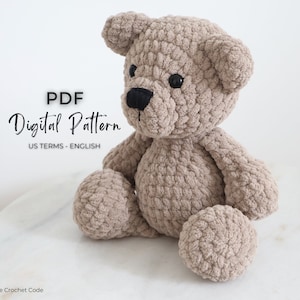 May include: A crocheted teddy bear sitting on a white marble surface. The bear is beige and has black eyes and a black nose. The text "PDF Digital Pattern US TERMS - ENGLISH" is visible in the image.