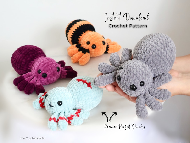Being held in the foreground is a foggy grey single toned crochet spider looking forwards. It lays infront of 3 other spiders. Each made with a unique colour change crochet combination