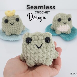 May include: Three handmade crochet frog toys in shades of green, each with large black eyes and a smiling mouth. One frog wears a yellow crown. The frogs sit on blue lily pads. The text "Seamless Crochet Design" is above the frogs.