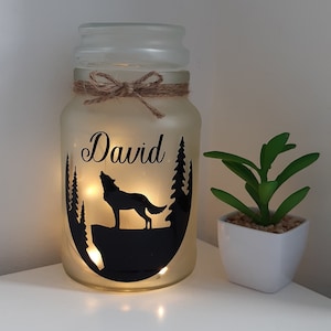 May include: A frosted glass jar with a brown twine bow, a wolf silhouette, and the name "David" in black lettering. The jar is lit from within, creating a warm glow.
