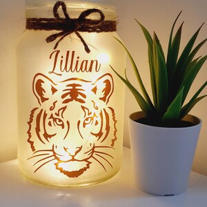 May include: A white frosted glass jar with a brown twine bow and a copper tiger silhouette. The jar is lit from within with white fairy lights and the name "Lillian" is written in copper lettering on the front.