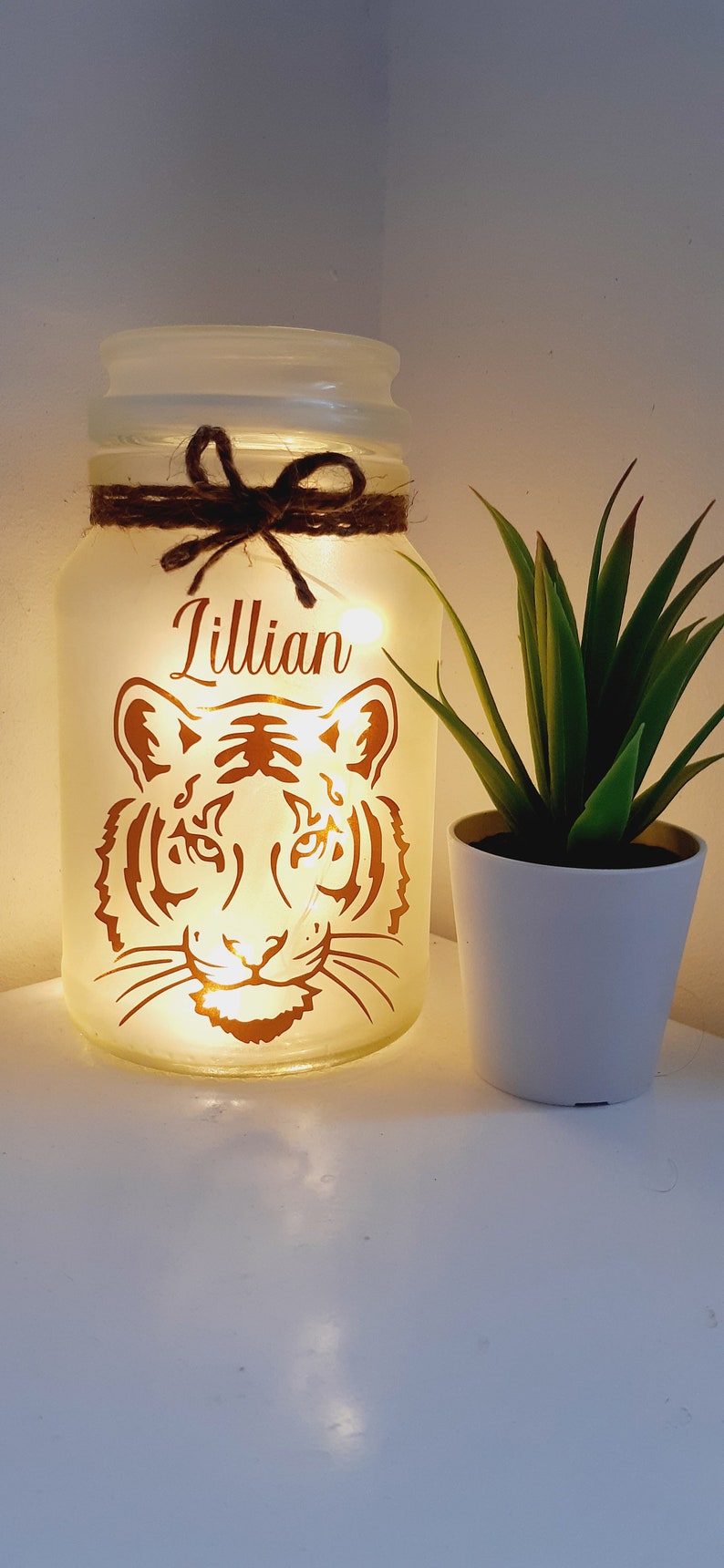 May include: A white frosted glass jar with a brown twine bow and a copper tiger silhouette. The jar is lit from within with white fairy lights and the name "Lillian" is written in copper lettering on the front.