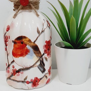 May include: White ceramic vase with a robin bird and red berries design. The vase has a rustic twine bow around the top.
