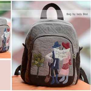 May include: Gray and brown backpack with a quilted design. Features a whimsical applique of two figures holding a sign that reads "Garden Plan." The backpack has a top handle, adjustable straps, and side pockets. Size L: 11.8" x 11" x 5.5".