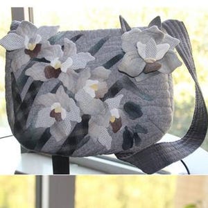 Può includere: Tre borse a mano in tessuto grigio con decorazioni floreali. Le borse sono realizzate in tessuto trapuntato e presentano fiori applicati in tonalità di bianco e grigio. Le borse hanno forme e dimensioni diverse, tra cui una piccola pochette, una borsa di medie dimensioni e una grande borsa a tracolla.