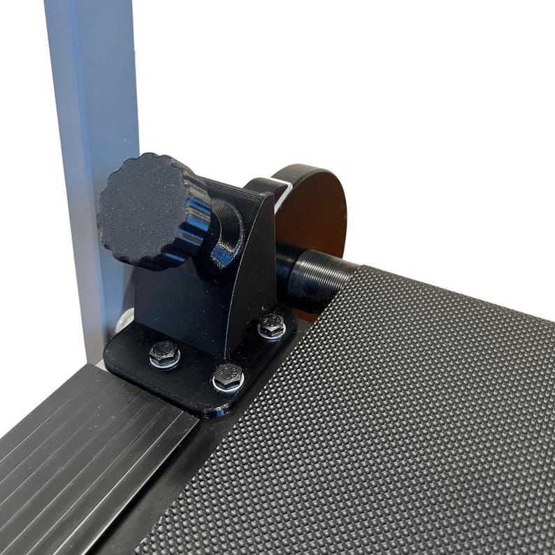 May include: Close-up of a black metal component with a textured knob and several bolts. The component is attached to a gray metal frame and a black, textured surface. The image is well-lit, highlighting the details of the mechanical parts.