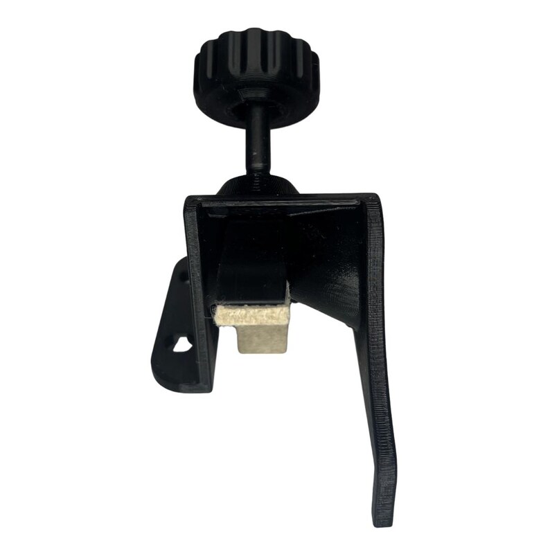May include: A black clamp with a textured knob and a padded contact surface. The clamp has a lever arm and a rectangular body. The knob is ribbed for grip.