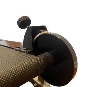 May include: Close-up of a black exercise machine component. The image shows a textured handle, a black circular disc, and a black knob. The machine appears to be made of metal.