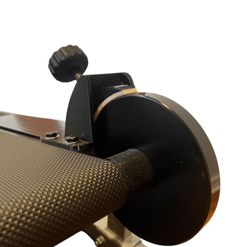 May include: Close-up of a black exercise machine component. The image shows a textured handle, a black circular disc, and a black knob. The machine appears to be made of metal.